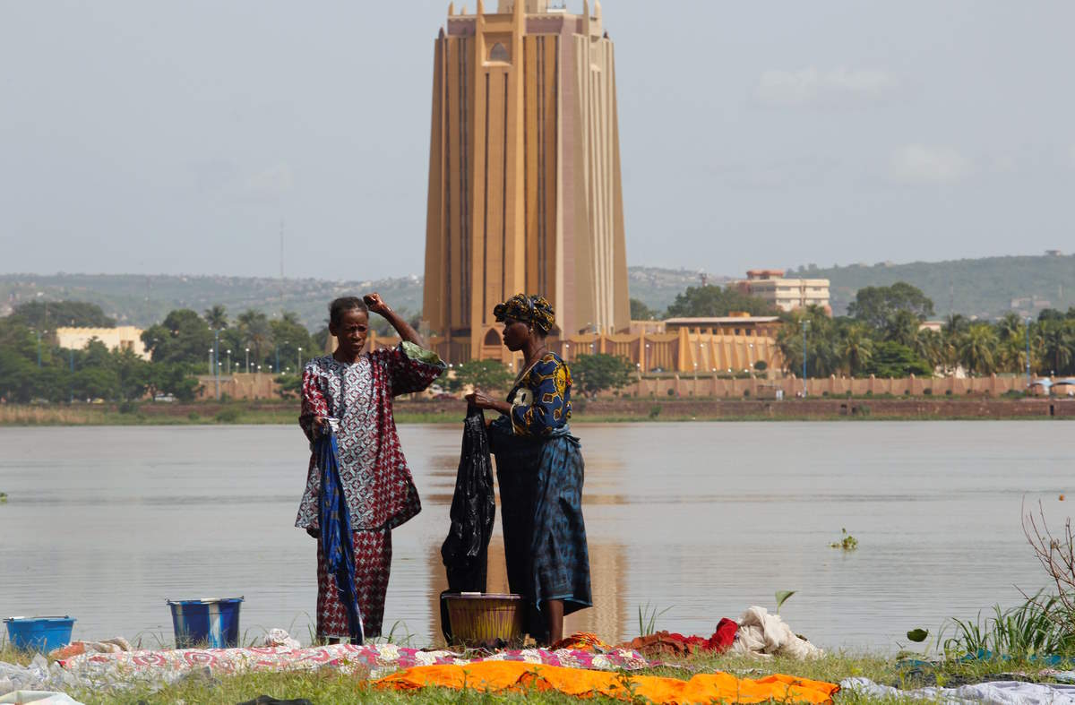 Women sort out clothing after doing their washing in the Niger River, with the headquarters of Central Bank of West African States in the background, in Bamako